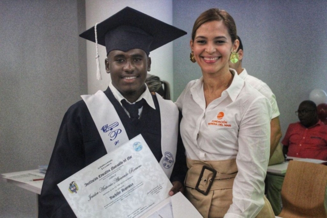 Jaider Alvarado recibe diploma de bachiller de parte de Isabel Mathieu, directora social de la fundación.